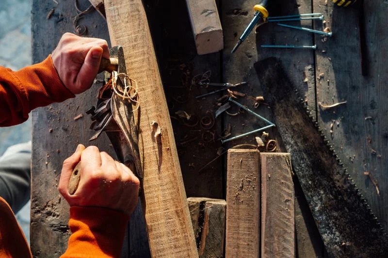 Hands using a plane on a long, thin piece of wood on a woodworking bench