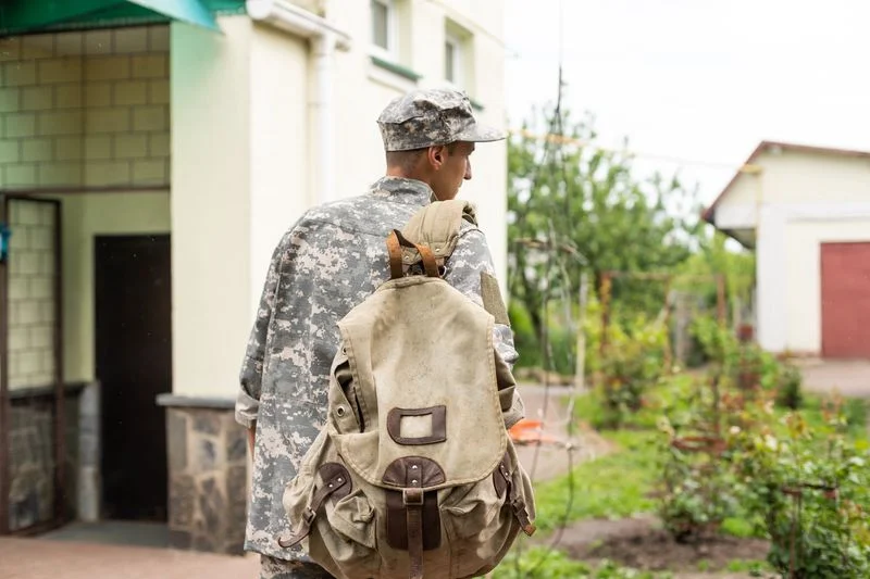 A man in an army uniform with a backpack outside a public building