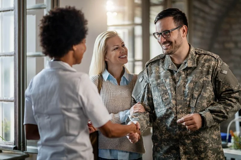 An AI image of a man with glasses and an army uniform shaking a woman's hand in an office, his wife next to him