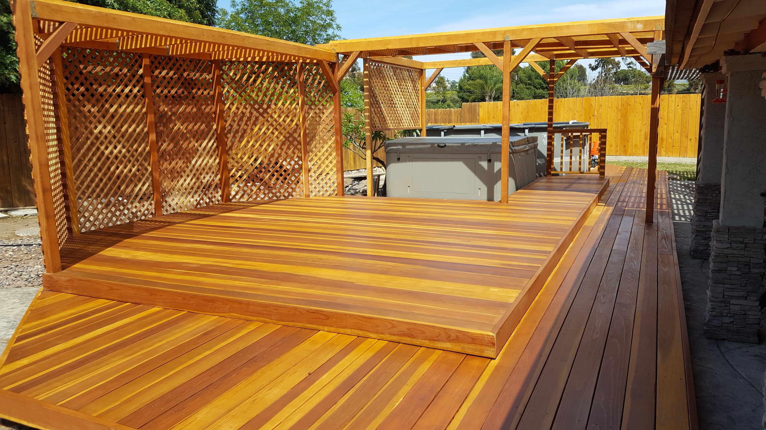 A two-tiered deck made of light brown, orangish wood with a hot tub