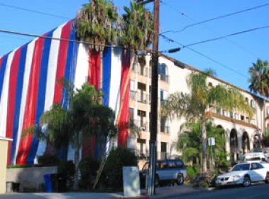An apartment complex half-covered by a large, striped fumigation tent
