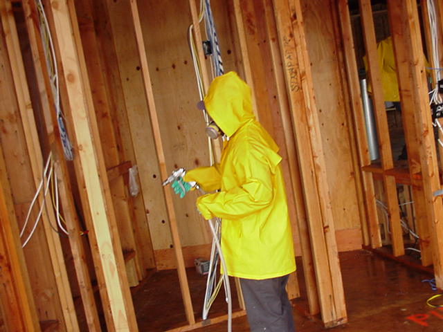 A professional in a yellow poncho spraying a new, half-built wall with pesticide